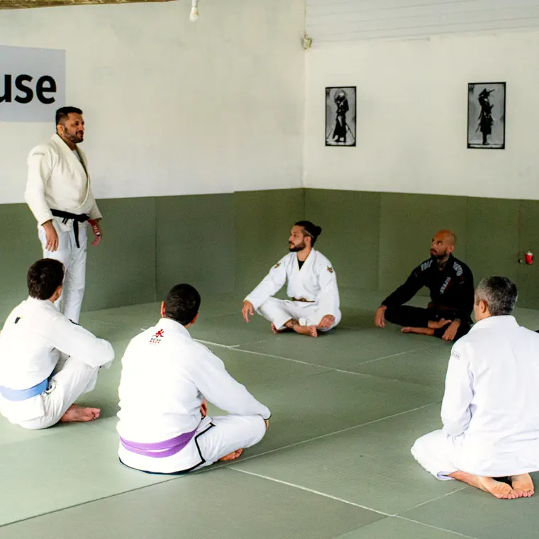 Turma sentada em roda no tatame da Jitshouse, durante a explicação da aula.