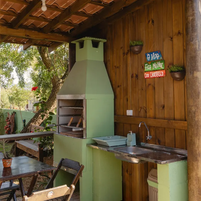 Área externa com churrasqueira, pia e mesa de madeira sob a varanda.