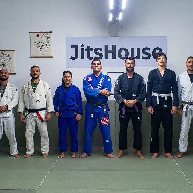 Turma inteira enfileirada no tatame, de kimono e sem kimono, sob o painel da JitsHouse.