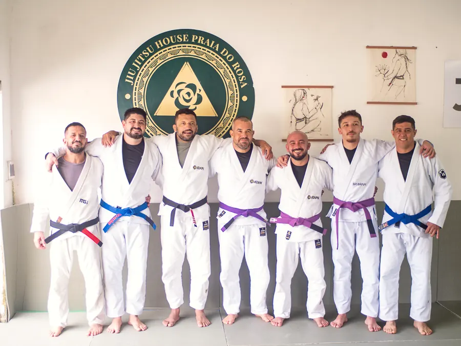 Alunos graduados enfileirados de kimono, com as faixas novas, diante do selo da casa.
