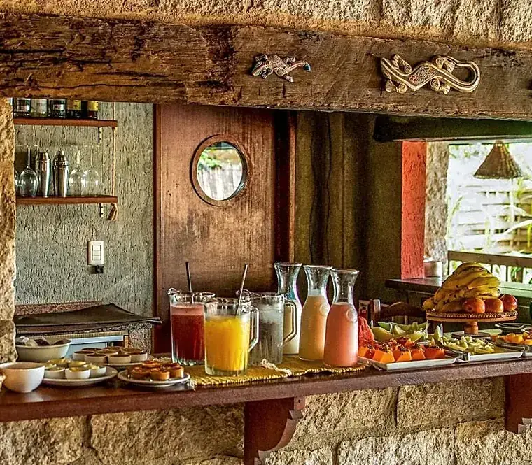 Mesa do café da manhã com frutas, pães e sucos servidos na casa.
