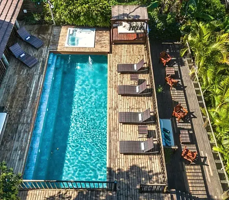 Vista aérea da piscina e do deck de madeira da casa, cercados pela mata.